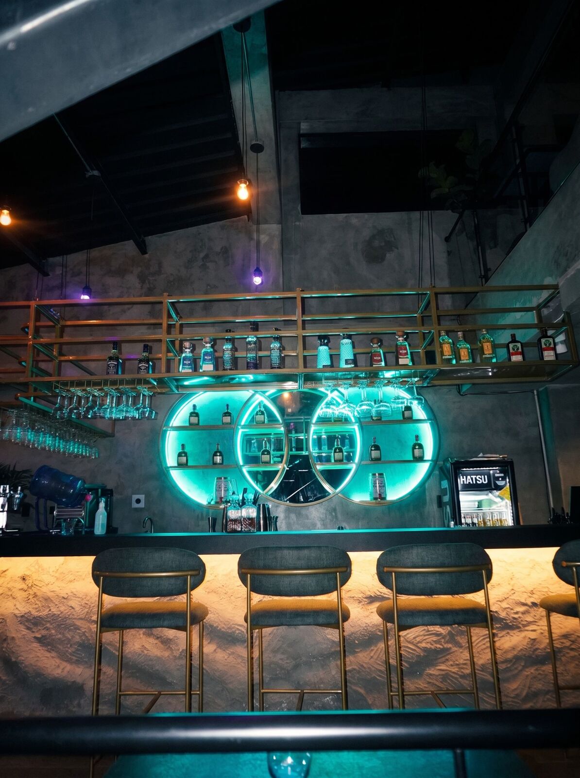 La barra de Alquimia: tres círculos de luz turquesa con las botellas y las copas colgadas